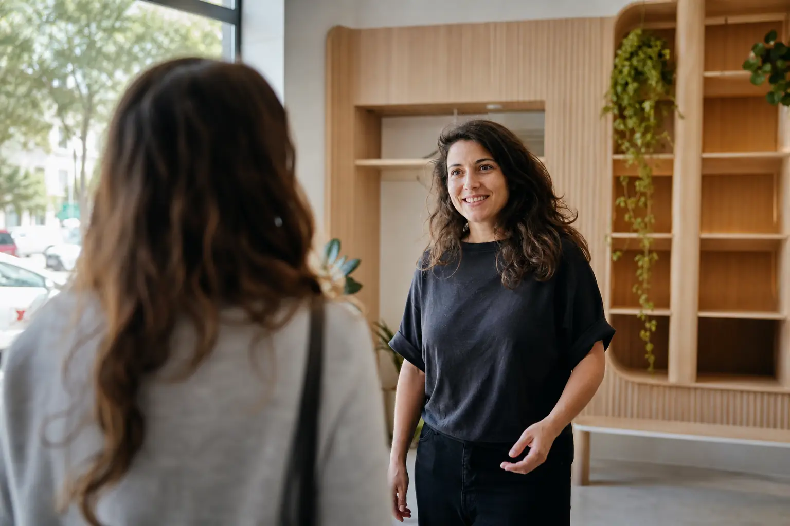 Une conseillère accueille une cliente dans une boutique claire au mobilier en bois