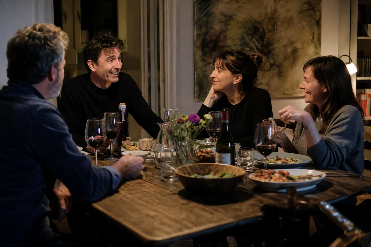 Quatre adultes partagent un repas autour d'une grande table dans un appartement