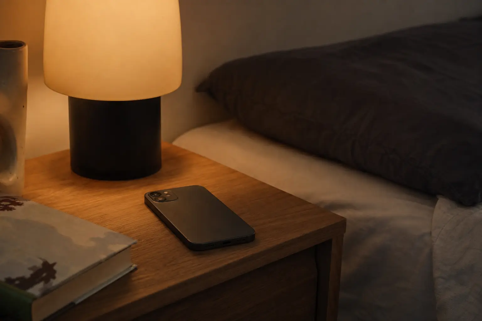 Un téléphone posé sur une table de nuit à côté d'une lampe allumée