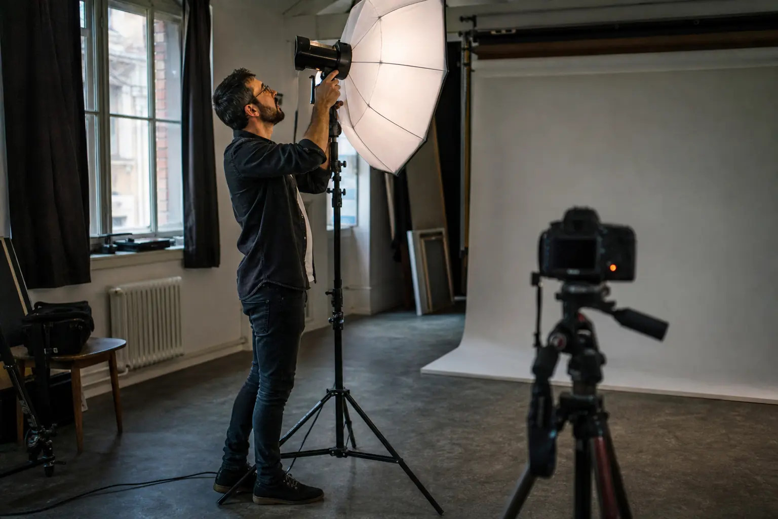 Un photographe règle un éclairage de studio devant un fond neutre