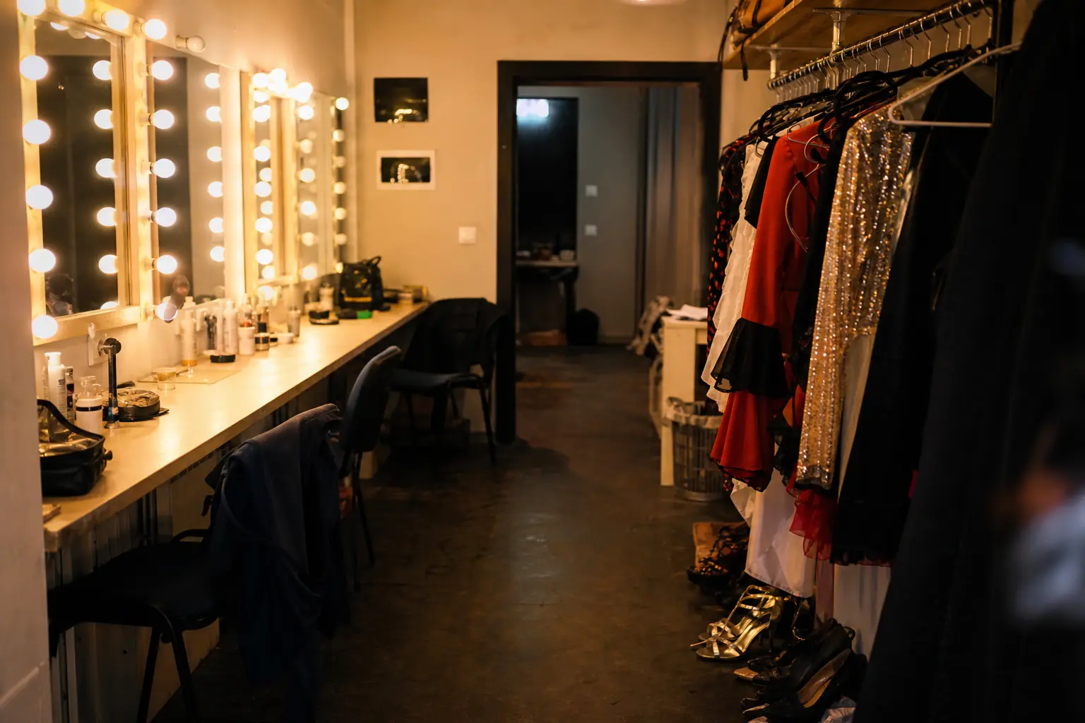 Loges d'un cabaret, miroirs éclairés et costumes suspendus, avant le spectacle