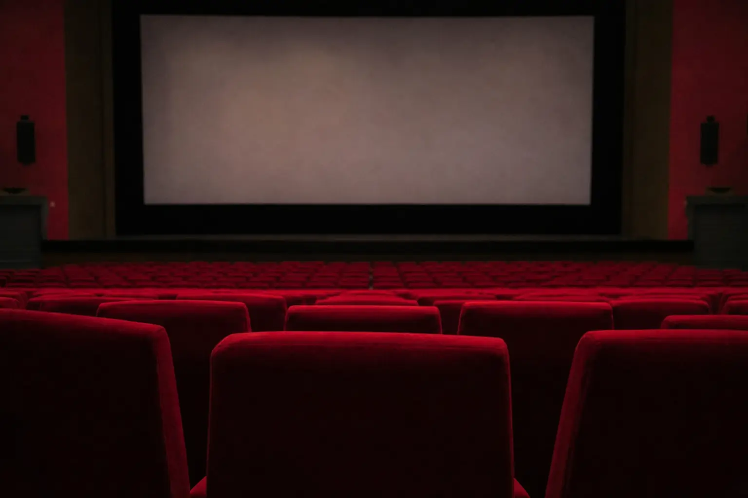 Un fauteuil de cinéma et un écran éteint, dans une salle vide