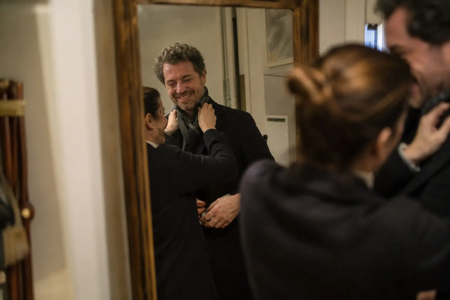 Un couple adulte se prépare pour sortir, dans le miroir d'une entrée, complice