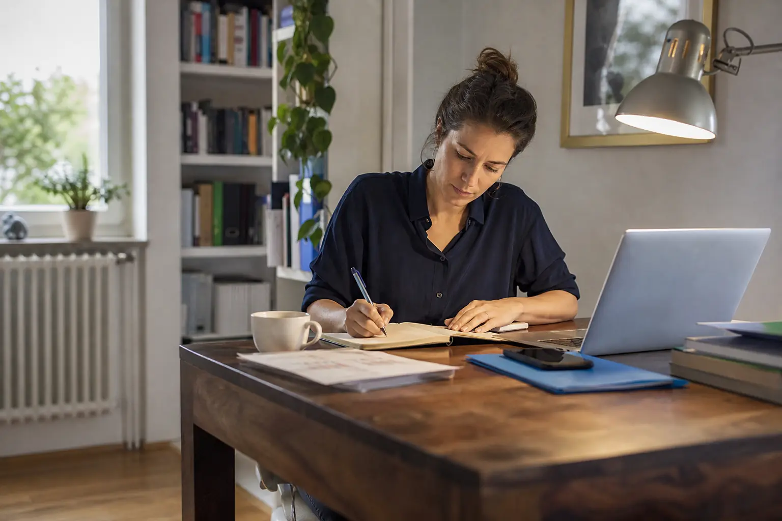 Une personne adulte travaille sur un ordinateur portable, prenant des notes dans un carnet
