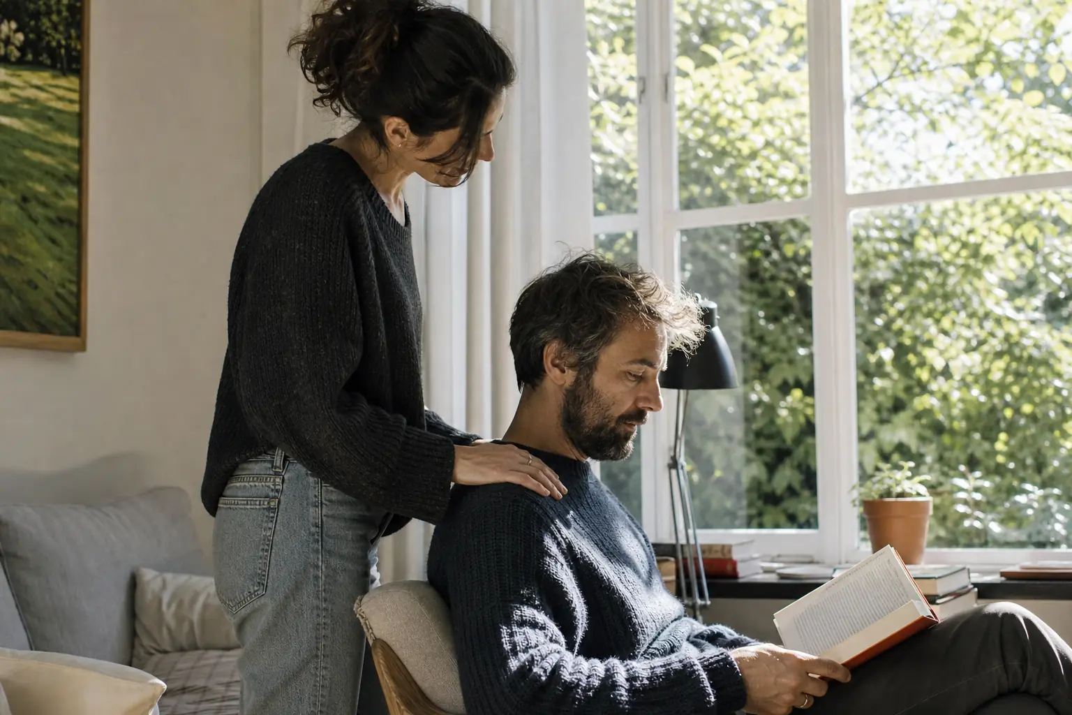 Une femme adulte pose la main sur l'épaule de son partenaire assis près d'une fenêtre