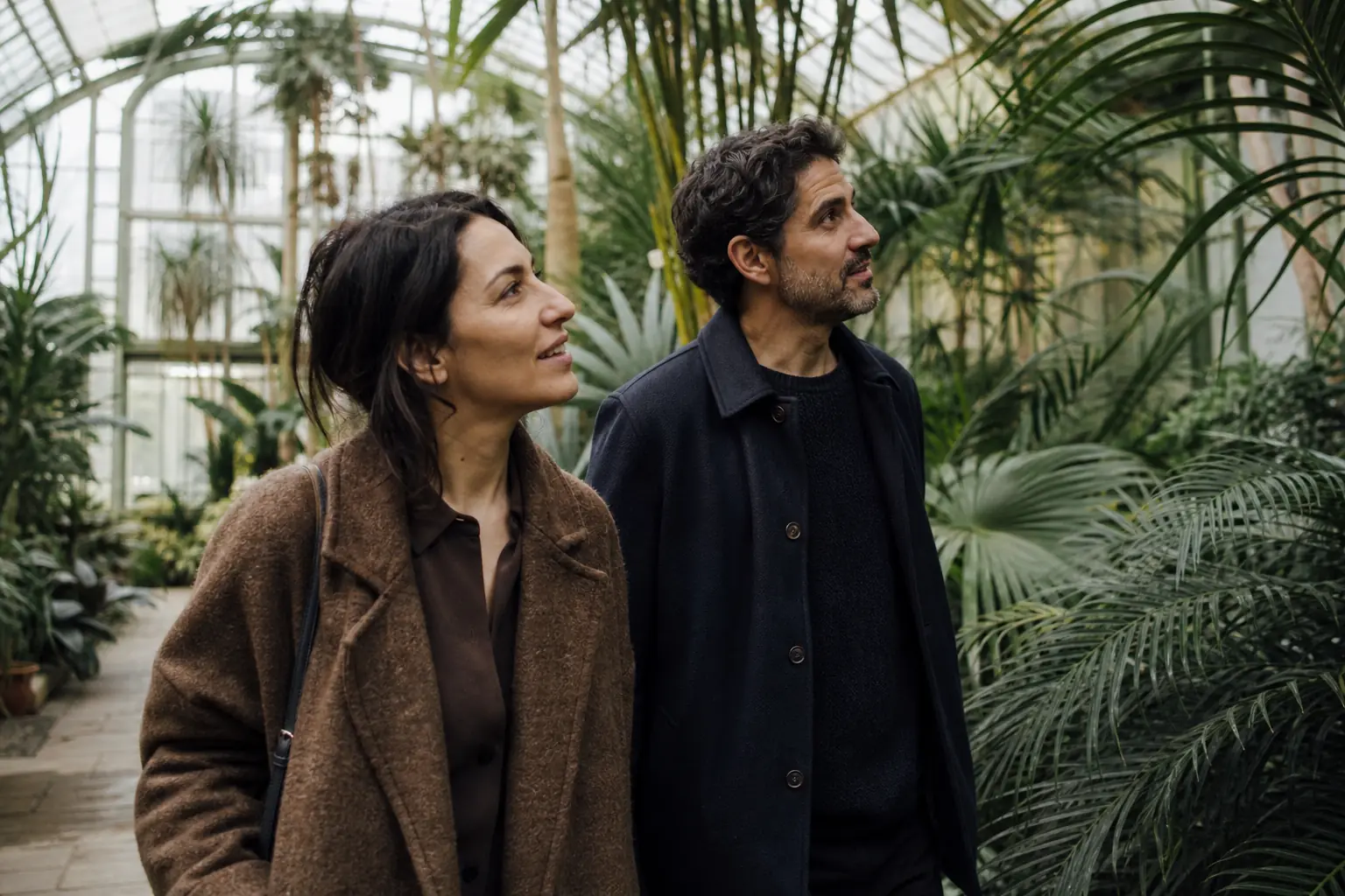 Deux adultes marchent dans une serre tropicale, entourés de plantes, lumière verte tamisée
